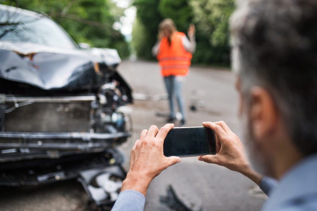 Unrecognizable man taking pictures of a broken car after an accident. Copy space. A female driver in the background.
